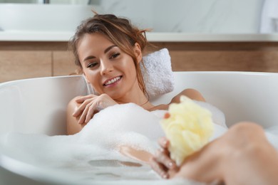 Beautiful woman with mesh sponge taking bath
