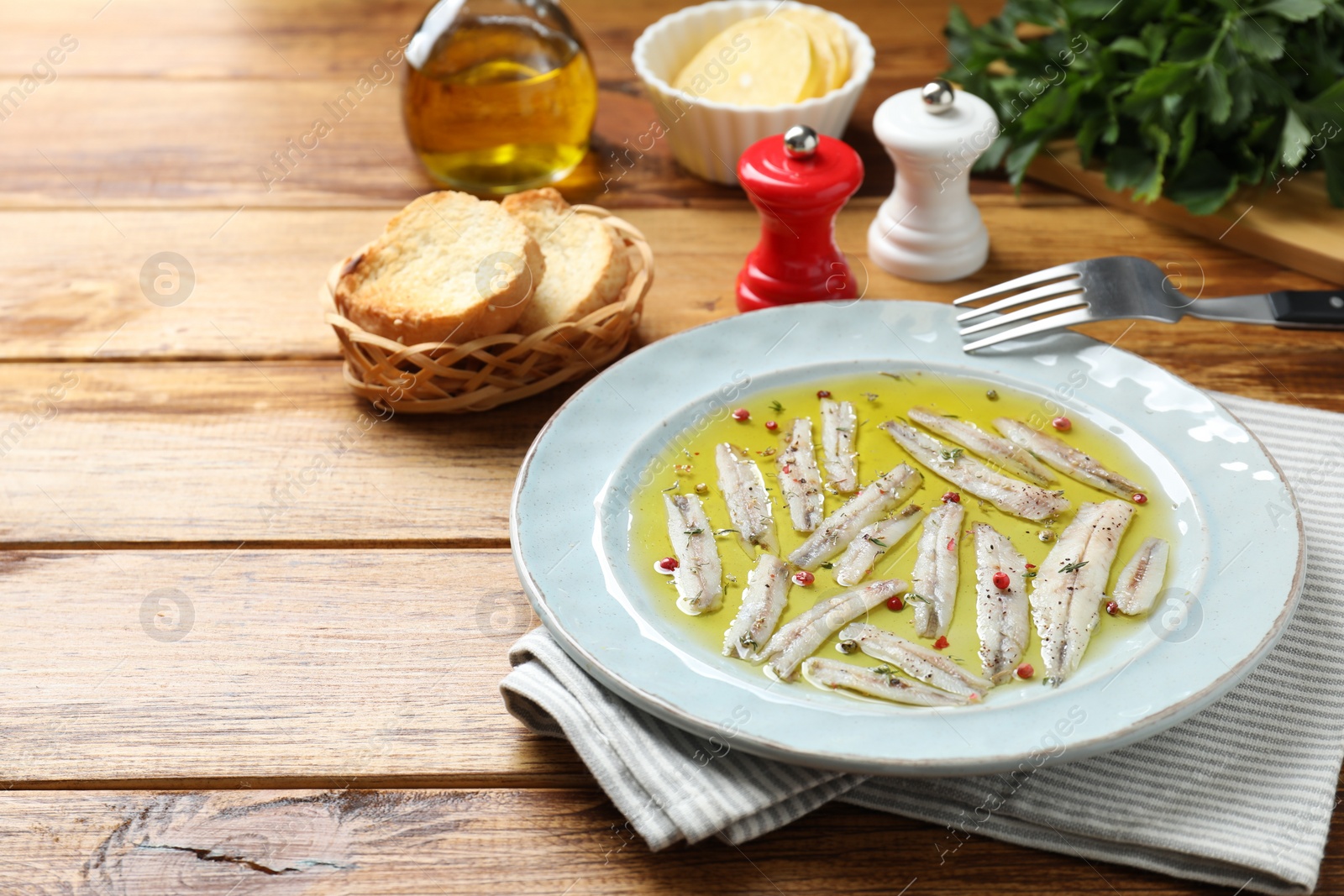 Photo of Tasty pickled anchovies with spices on wooden table. Space for text