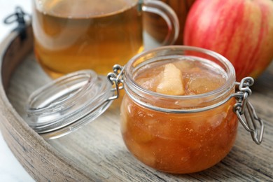 Photo of Delicious apple jam in jar on wooden tray, closeup