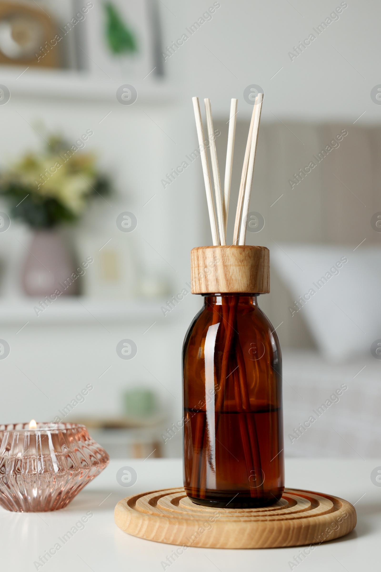 Photo of Aromatic reed air freshener and candle on white table in room