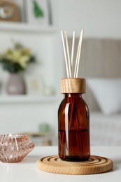 Aromatic reed air freshener and candle on white table in room