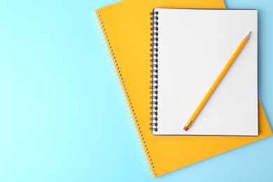 Notebooks with pencil on light blue background, top view. Space for text