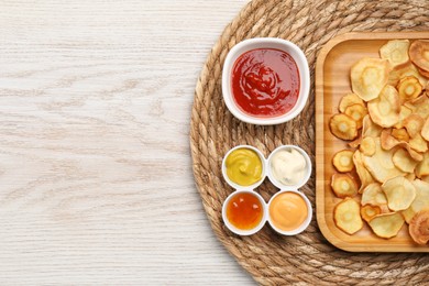 Tasty homemade parsnip chips with different sauces on white wooden table, flat lay. Space for text