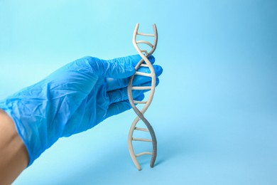 Scientist with DNA molecule model made of plasticine on light blue background, closeup