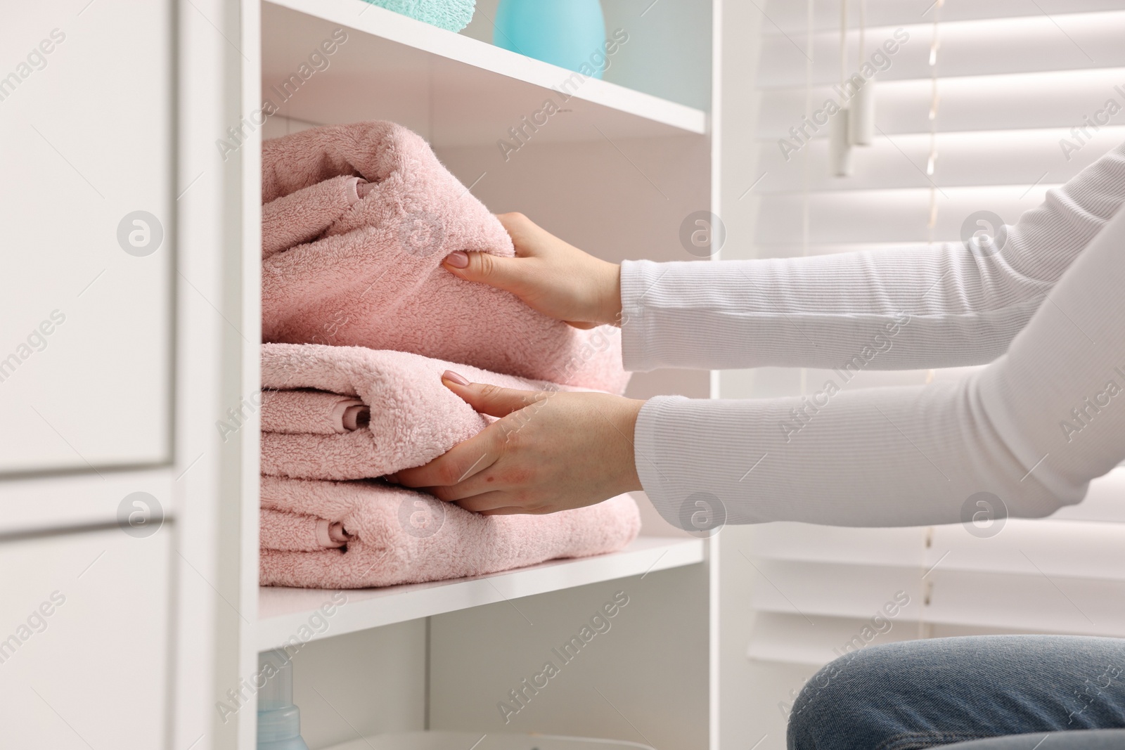 Photo of Woman stacking clean towels on shelf indoors, closeup