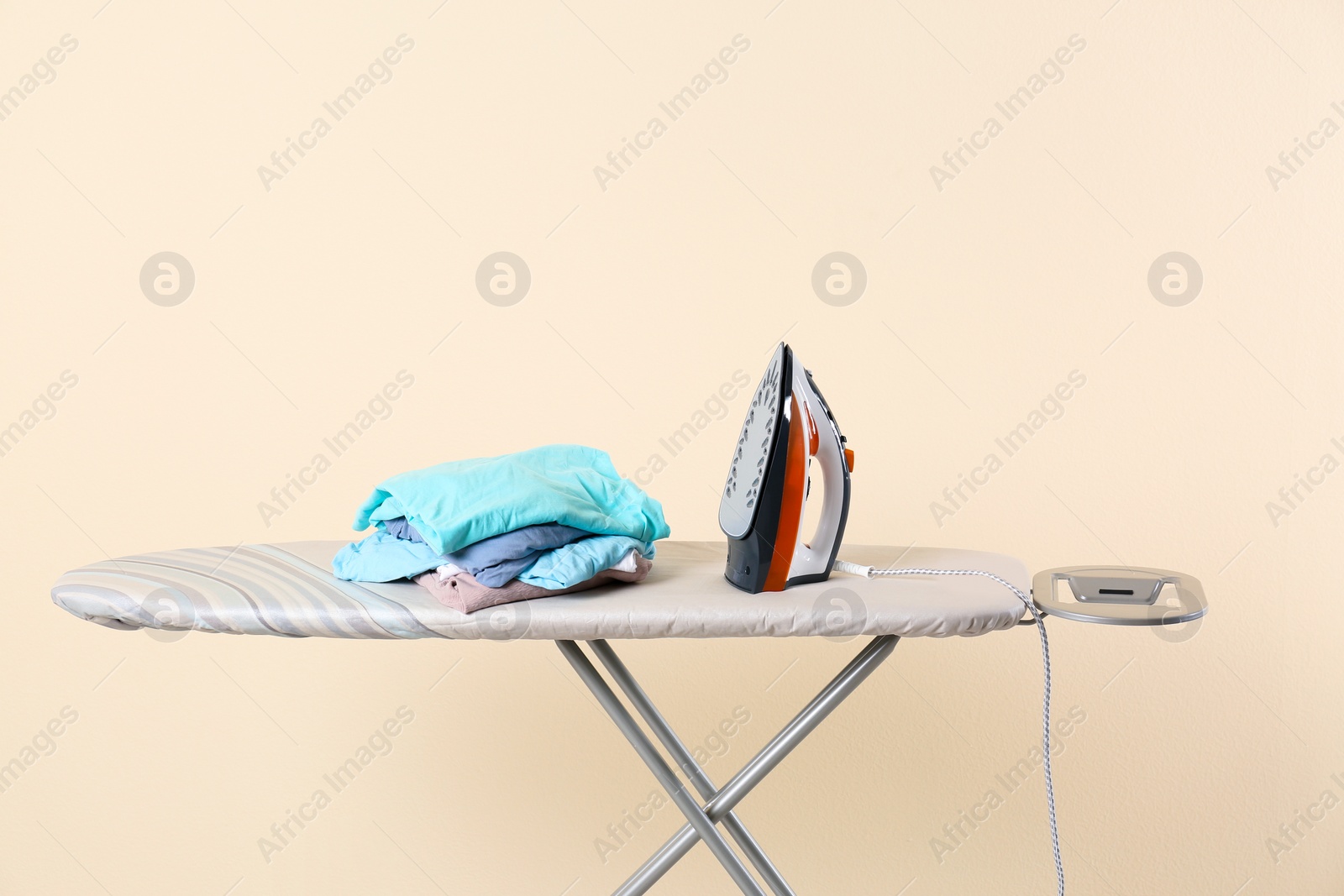 Photo of Board with modern iron and clean laundry on beige background