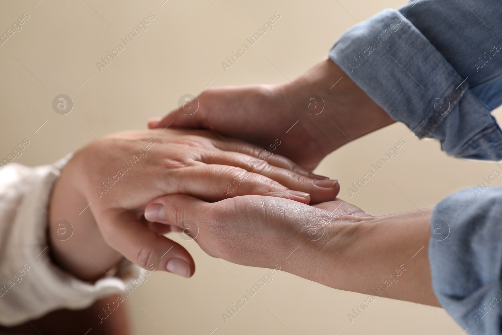 Photo of Woman holding hands with her mother on beige background, closeup