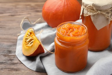 Photo of Jars of pumpkin jam and fresh pumpkins on wooden table, closeup