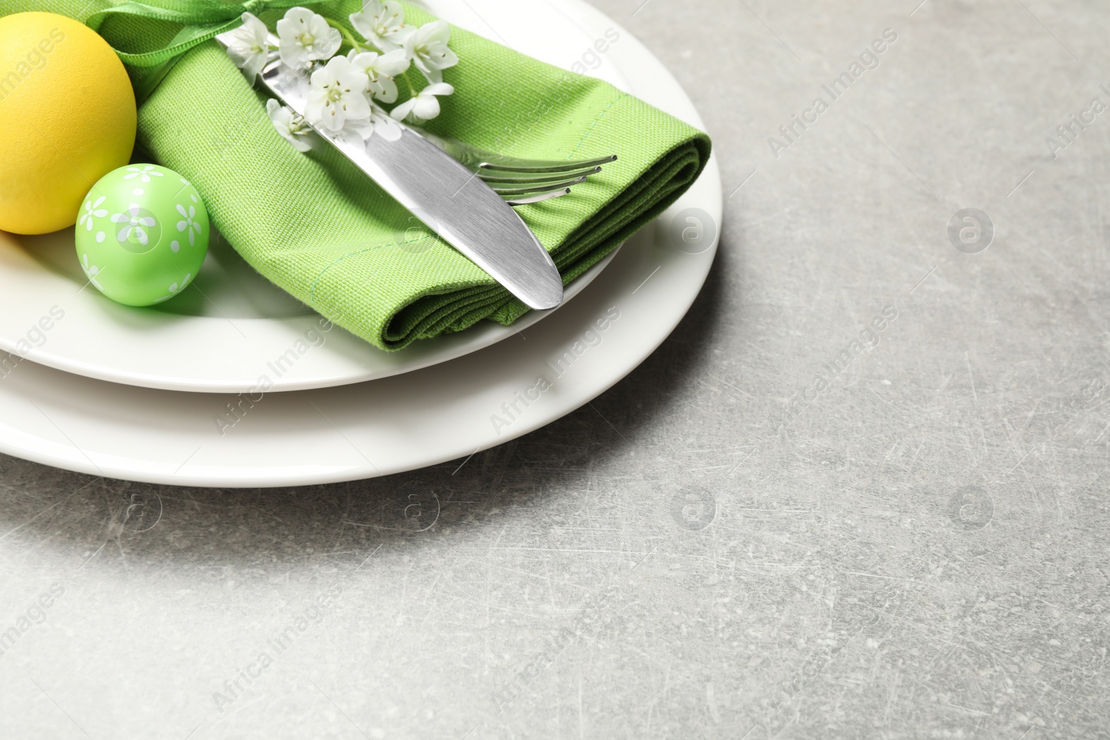 Photo of Festive Easter table setting with floral decor on grey background, closeup. Space for text