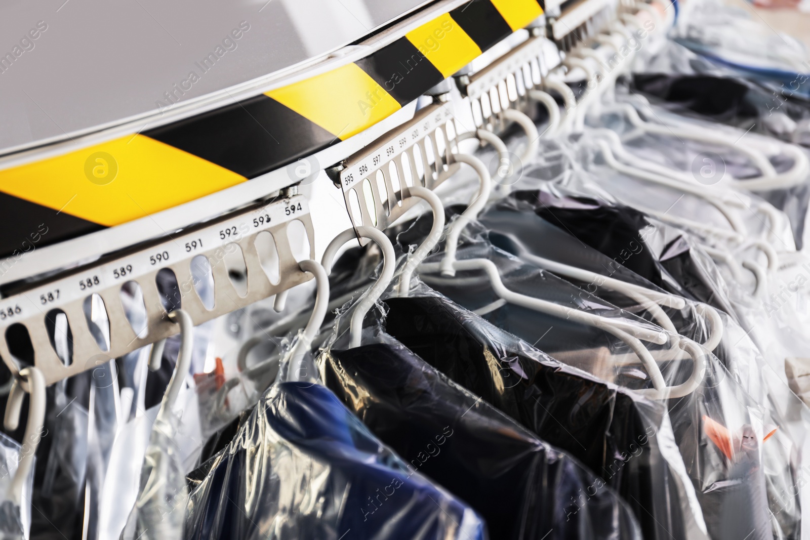 Photo of Hangers with clothes on garment conveyor at dry-cleaner's, closeup