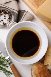 Photo of Bowl of balsamic vinegar with oil, bread and spices on white table, flat lay