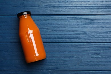 Healthy carrot juice in glass bottle on blue wooden table, top view. Space for text