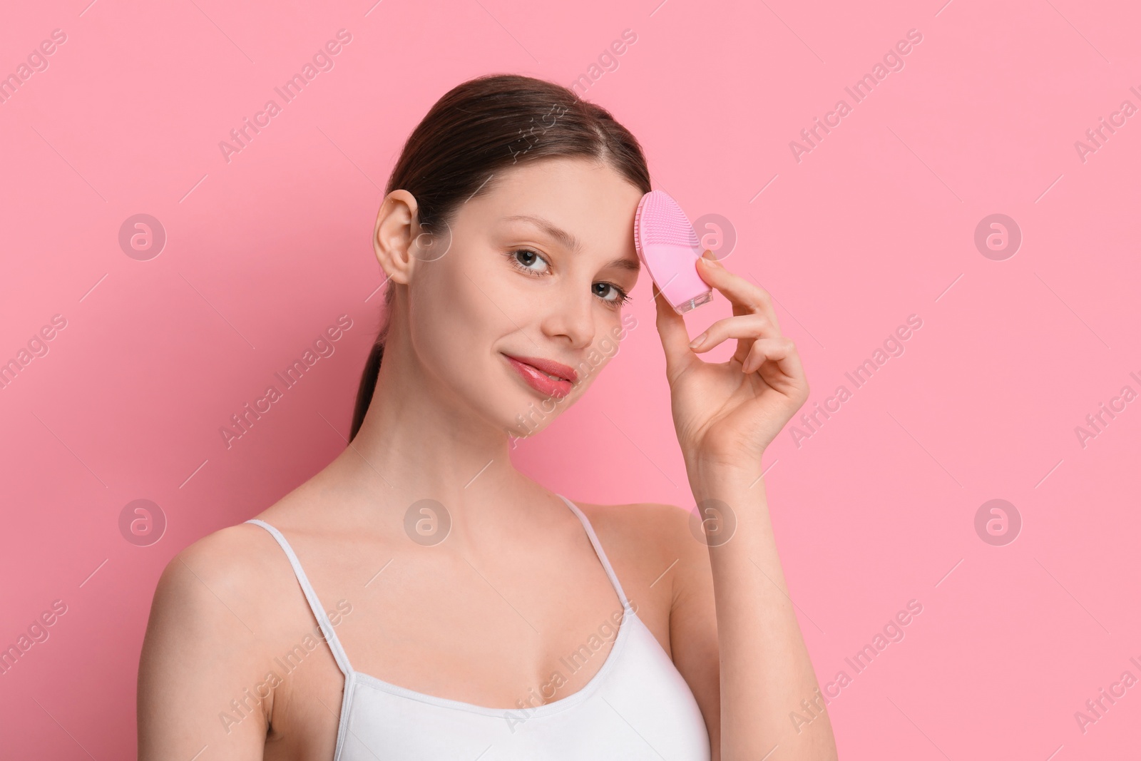 Photo of Washing face. Young woman with cleansing brush on pink background