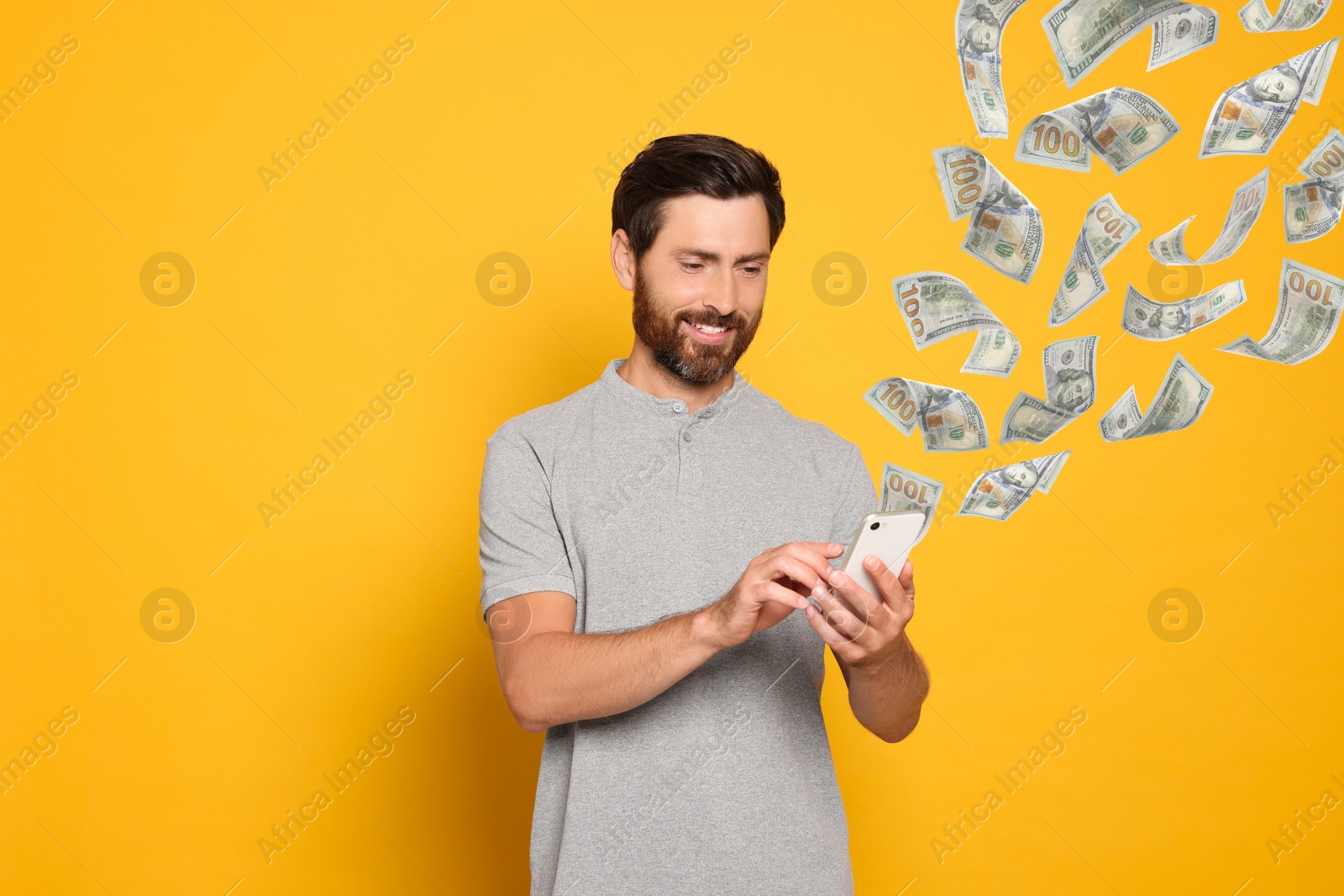 Image of Online payment. Man buying something using mobile phone on yellow background. Dollar banknotes flying out of gadget demonstrating process of money transaction