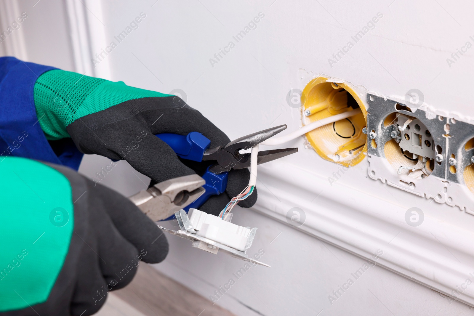 Photo of Professional repairman fixing power sockets with pliers indoors, closeup