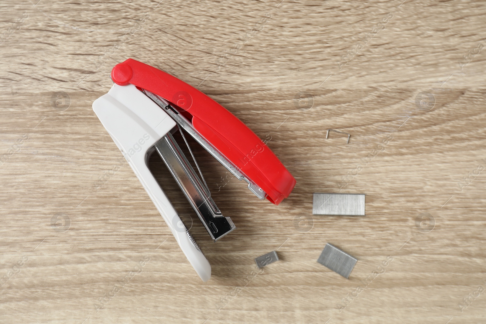 Photo of Bright stapler and metal staples on wooden table, top view