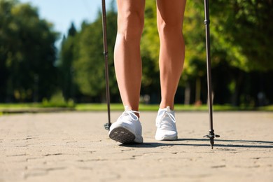 Woman practicing Nordic walking with poles in park on sunny day, closeup