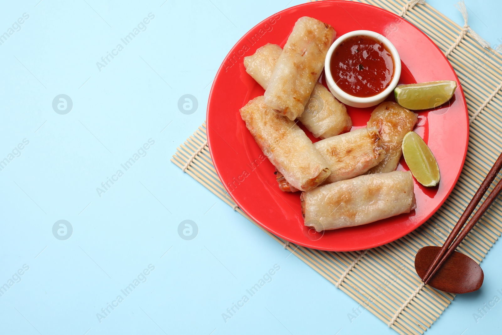 Photo of Tasty fried spring rolls, lime and sauce served on light blue table, top view. Space for text