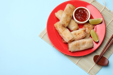 Photo of Tasty fried spring rolls, lime and sauce served on light blue table, top view. Space for text