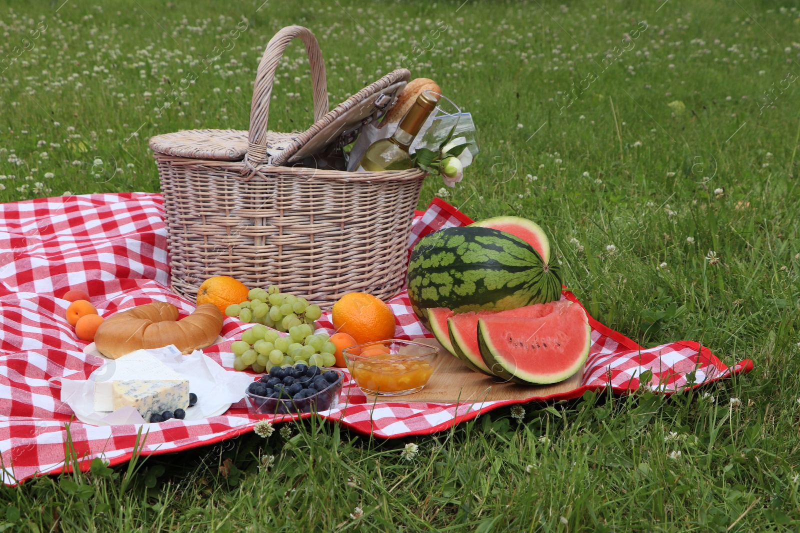 Photo of Picnic blanket with delicious food and wine outdoors on summer day