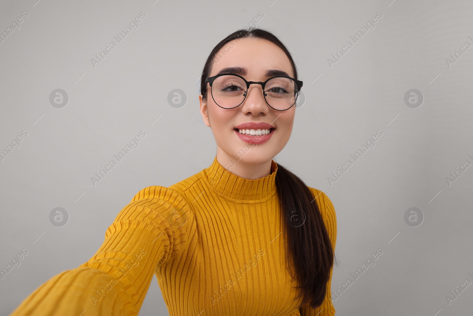 Photo of Smiling young woman taking selfie on grey background