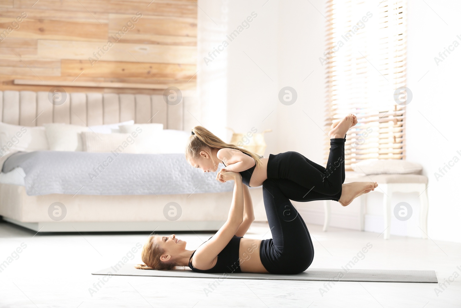 Photo of Mother and daughter in matching sportswear doing yoga together near bed at home