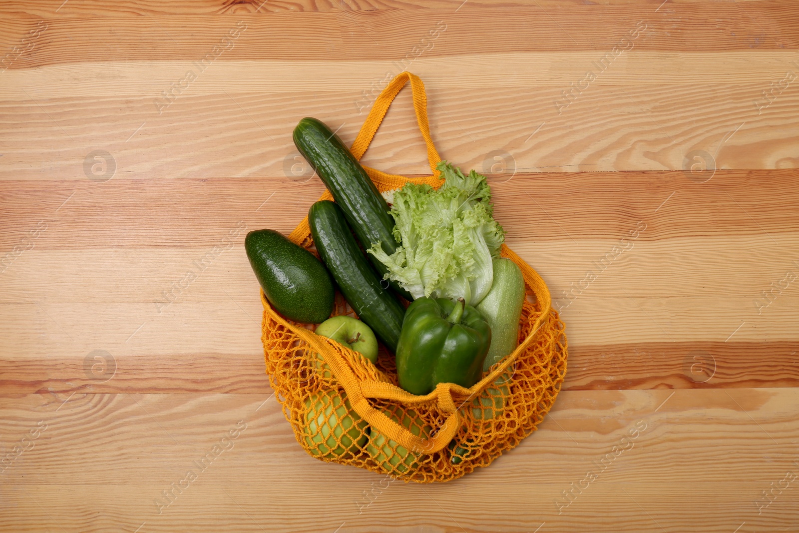 Photo of Orange net bag with vegetables and fruits on wooden background, top view