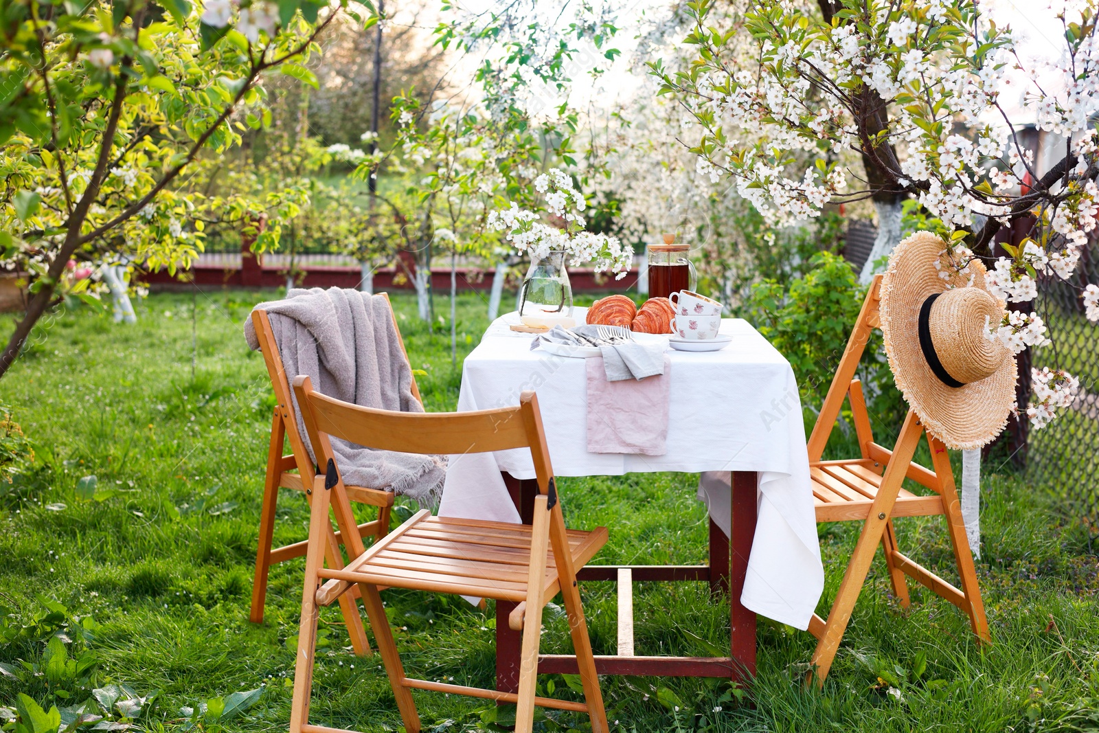 Photo of Stylish table setting with beautiful spring flowers, tea and croissants in garden