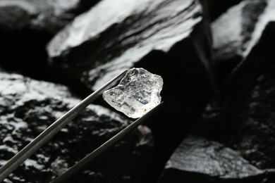 Photo of Tweezers with beautiful shiny diamond over stones, closeup