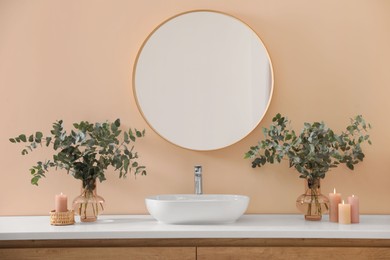 Stylish mirror, eucalyptus branches and vessel sink in modern bathroom. Interior design