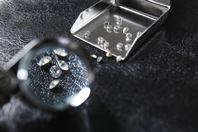 Photo of Precious jewels on black leather background, view through magnifier
