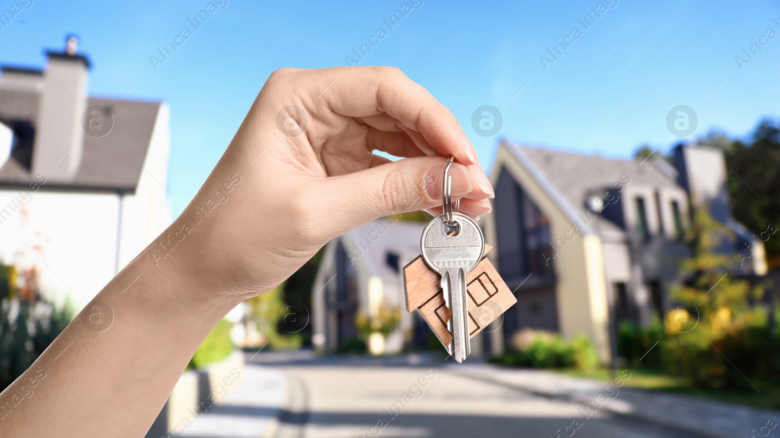 Image of Real estate agent holding key against modern houses, closeup. Banner design
