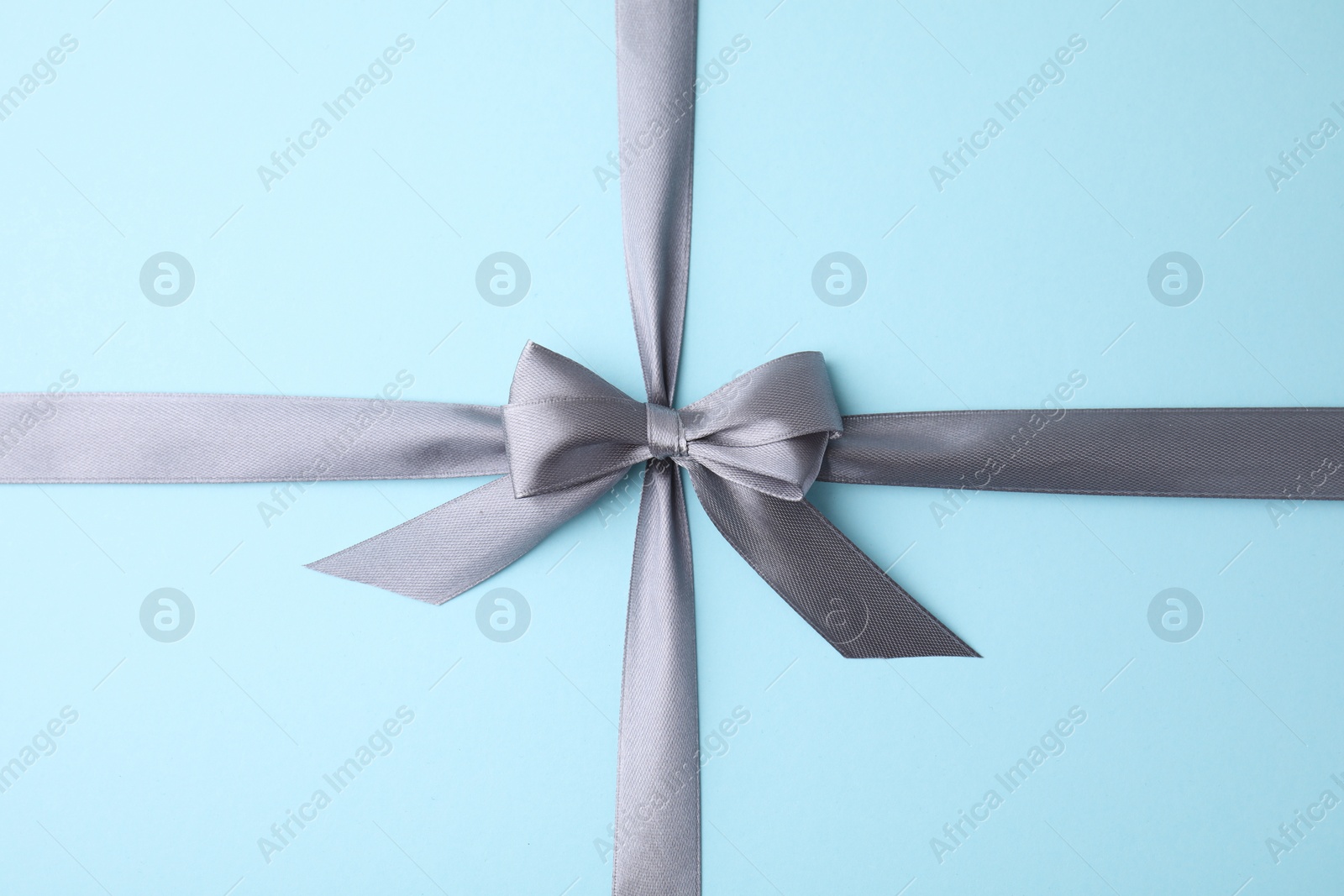 Photo of Grey satin ribbon with bow on light blue background, top view