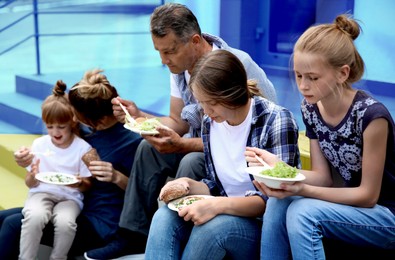 Image of Group of hungry people eating food with colors of Ukrainian flag on background. Helping refugees during war