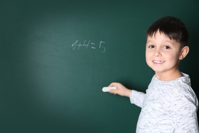 Child writing math sum on chalkboard. Space for text