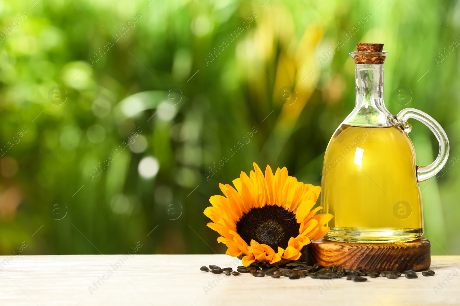 Photo of Sunflower cooking oil, seeds and yellow flower on white wooden table outdoors, space for text