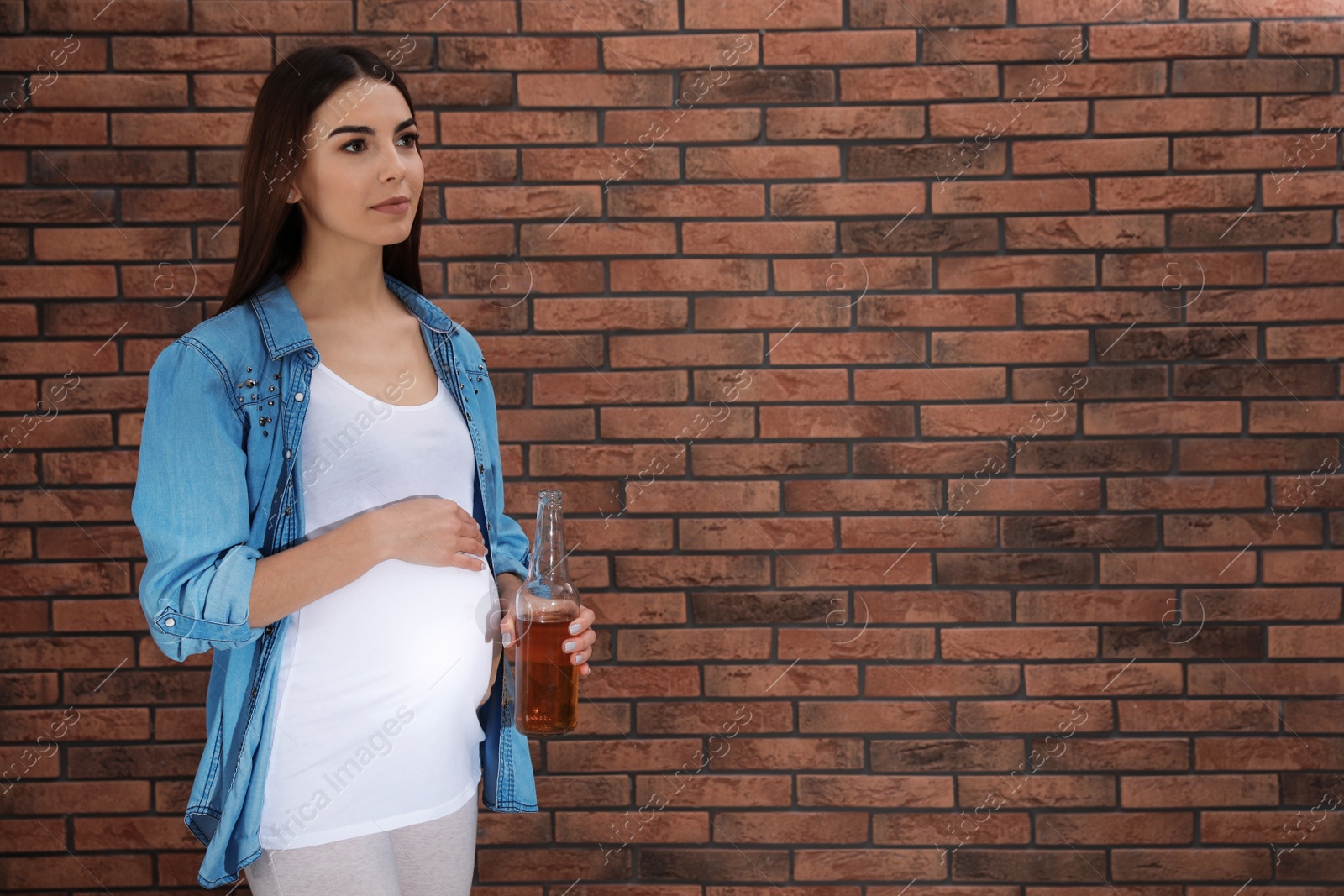 Photo of Future mother with bottle of alcohol drink against brick wall. Bad habits during pregnancy