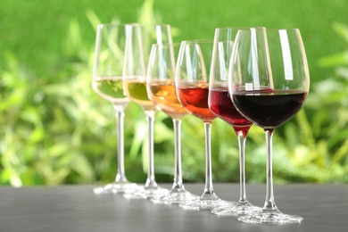 Row of glasses with different wines on grey table against blurred background. Space for text