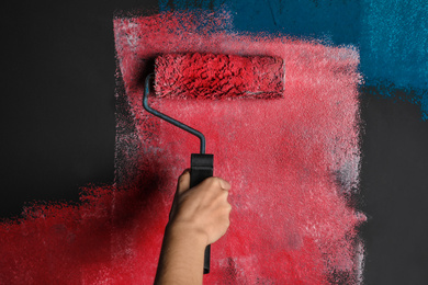 Photo of Woman painting grey wall with pink dye, closeup