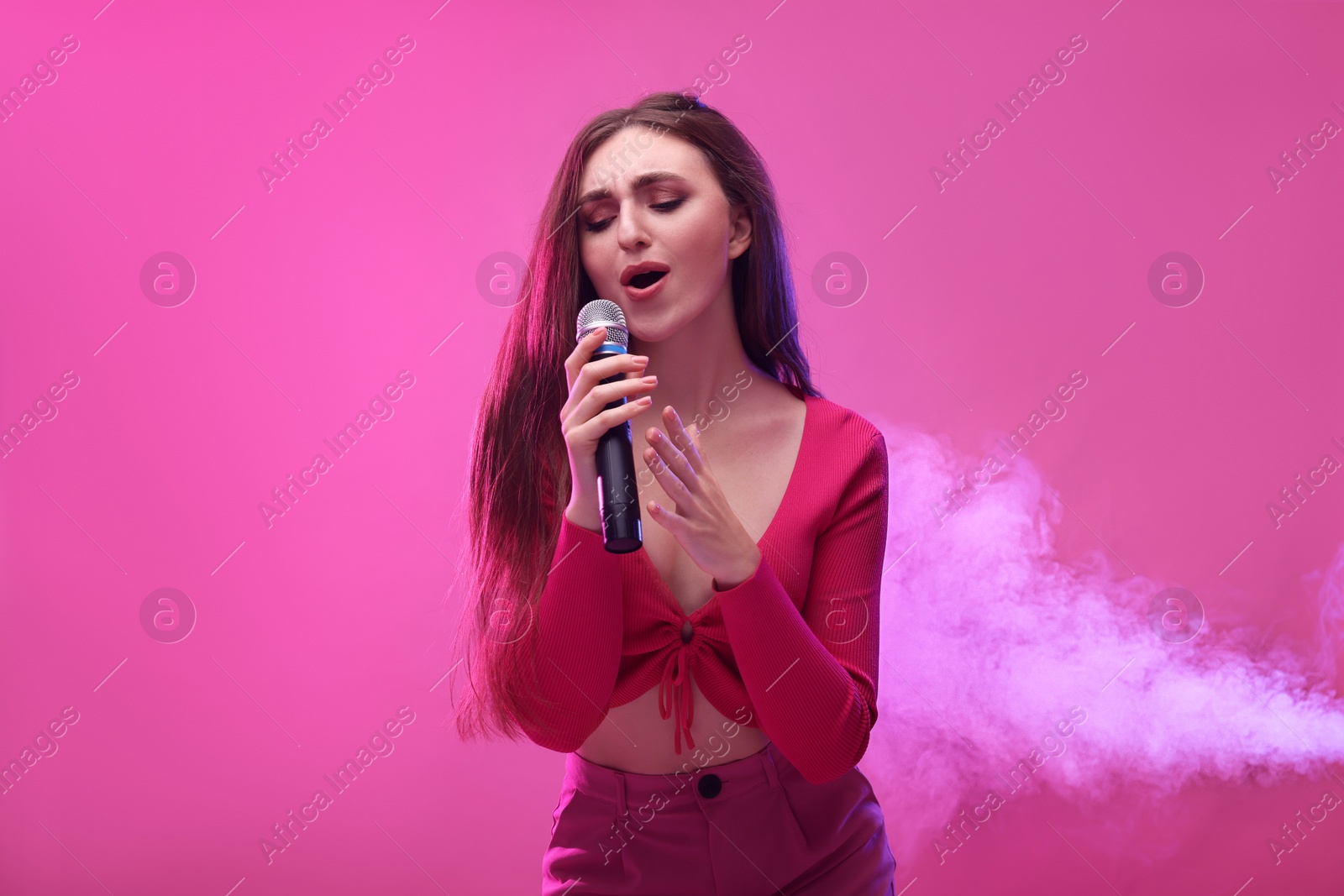 Photo of Emotional woman with microphone singing on pink background