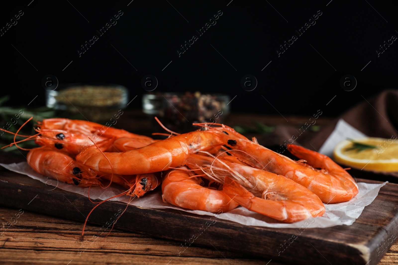 Photo of Delicious cooked shrimps on wooden table against black background