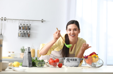 Young woman tasting delicious soup in kitchen