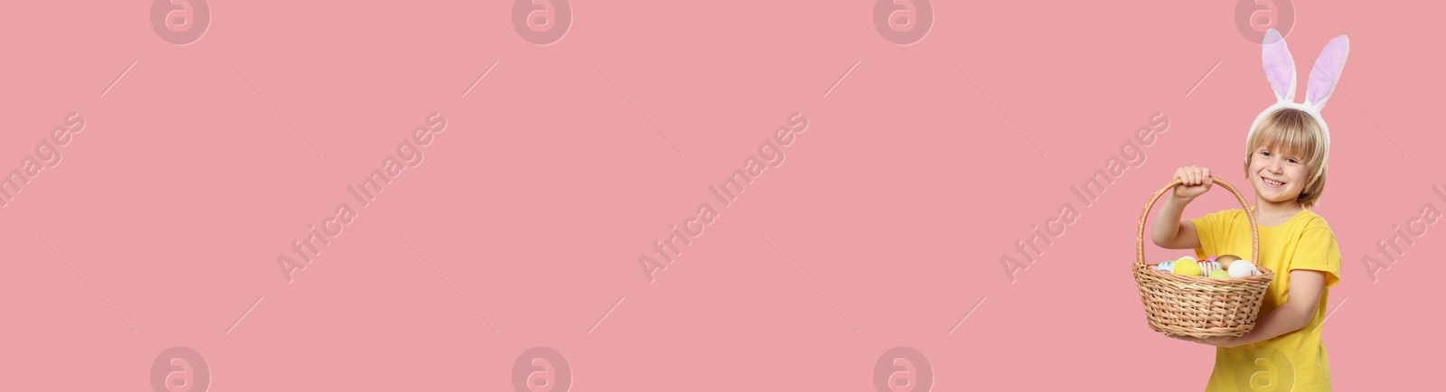 Image of Happy boy with bunny ears holding basket full of Easter eggs on pink background, space for text. Banner design