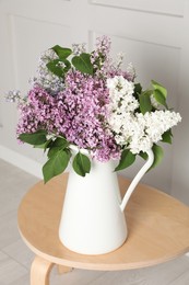 Photo of Beautiful lilac flowers in vase on wooden table near white wall
