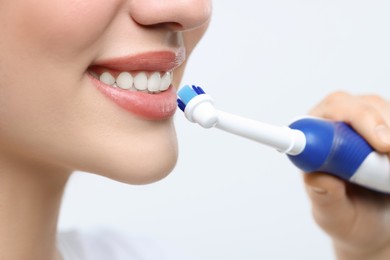 Woman brushing her teeth with electric toothbrush on white background, closeup