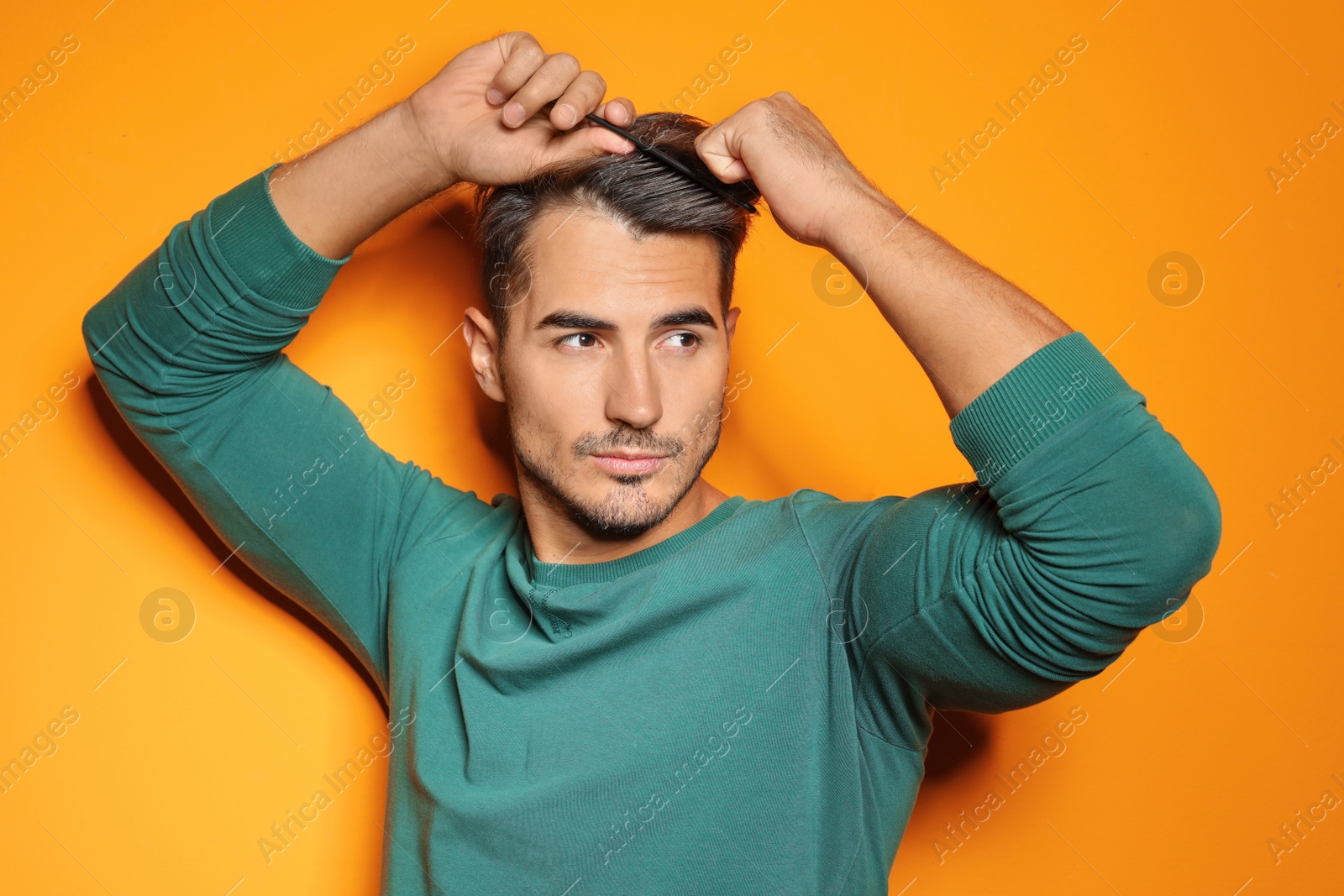 Photo of Young man with comb posing on color background. Trendy hairstyle