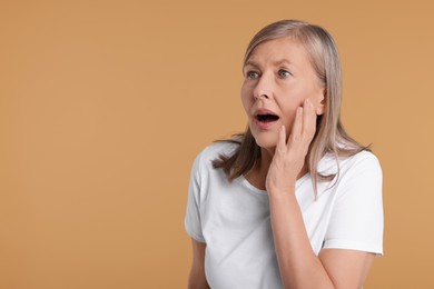 Portrait of surprised senior woman on beige background, space for text