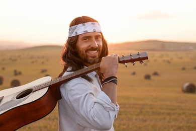 Photo of Portrait of happy hippie man with guitar in field