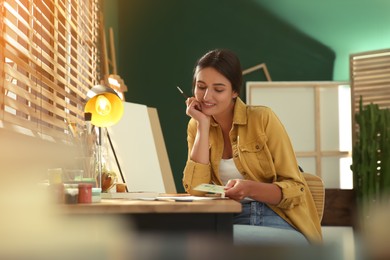 Photo of Young woman drawing on paper at table indoors