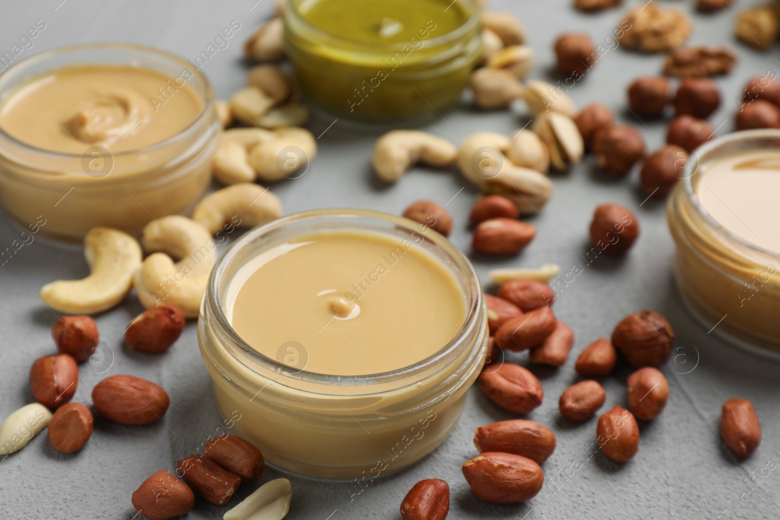 Photo of Jars with butters made of different nuts and ingredients on grey table, closeup